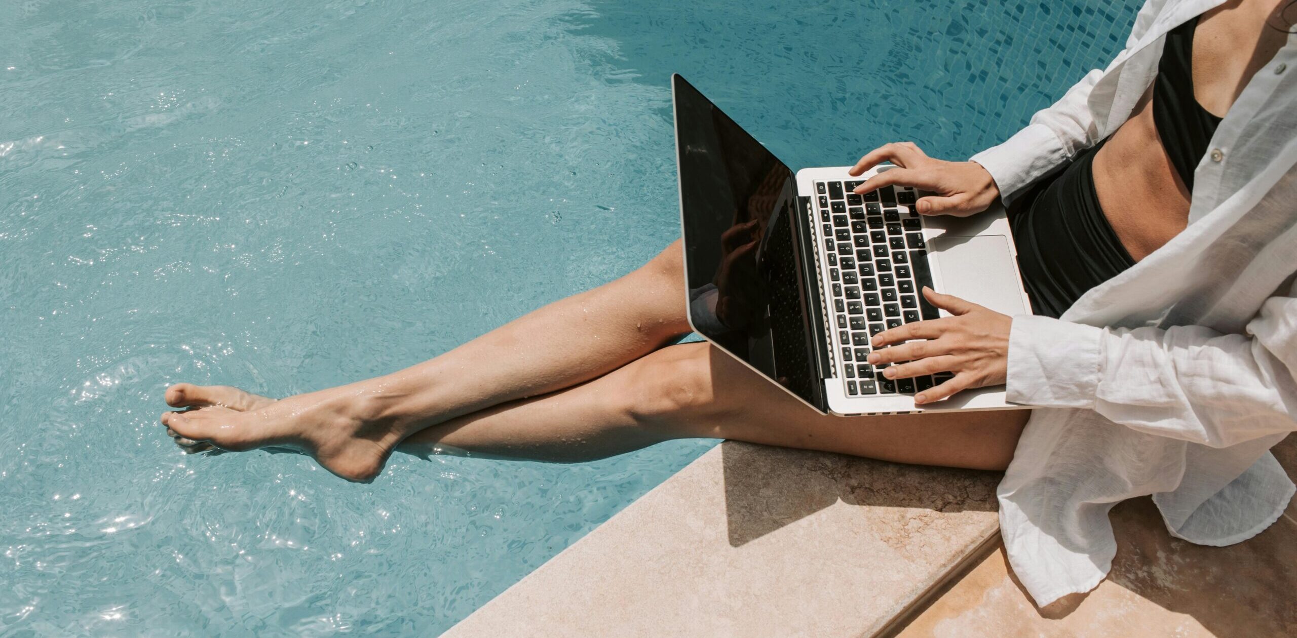 A woman working on a laptop near the pool